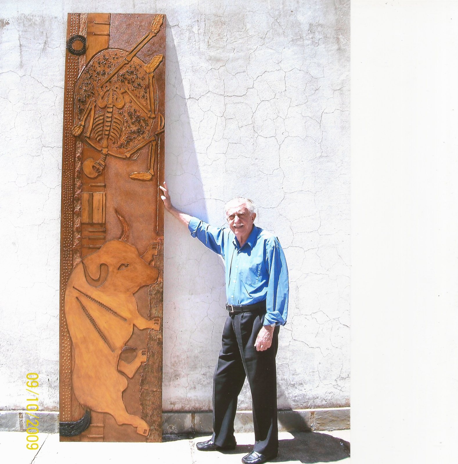 Juan José Cartasso, a los 85 años, de pie junto a una plancha de neograbado monumental más alta que él: un toro, un esqueleto sobre un disco y texturas en relieve sobre madera.