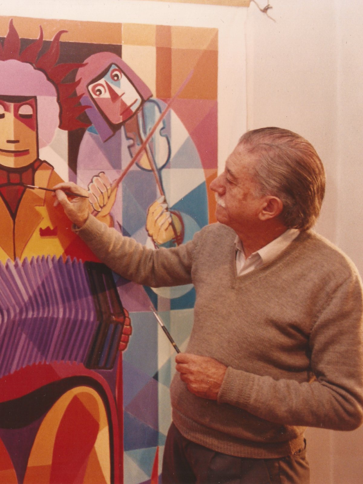 Juan José Cartasso, de perfil y con un pincel en cada mano, pintando un gran óleo de músicos de tango: un bandoneonista al centro y un violinista detrás.